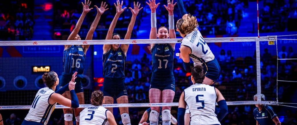 Professional women's volleyball match with players jumping at the net for a block and spike.