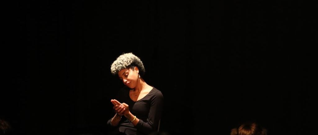 Una mujer afro con un vestido negro sentada en un escenario