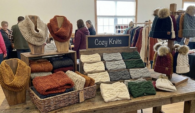 Sales table at a crafting show with knitted cowls and beanie caps