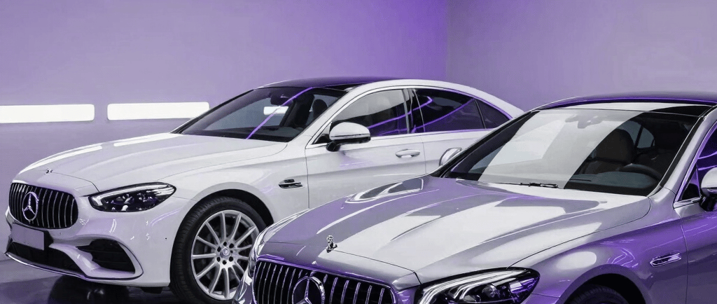 Silver and white Mercedes-Benz luxury sedans showcased in a modern showroom with purple ambient lighting.