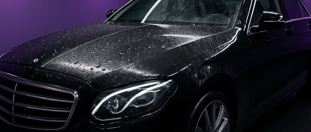 A shiny black luxury sedan with water droplets in a studio with purple walls and LED lighting.
