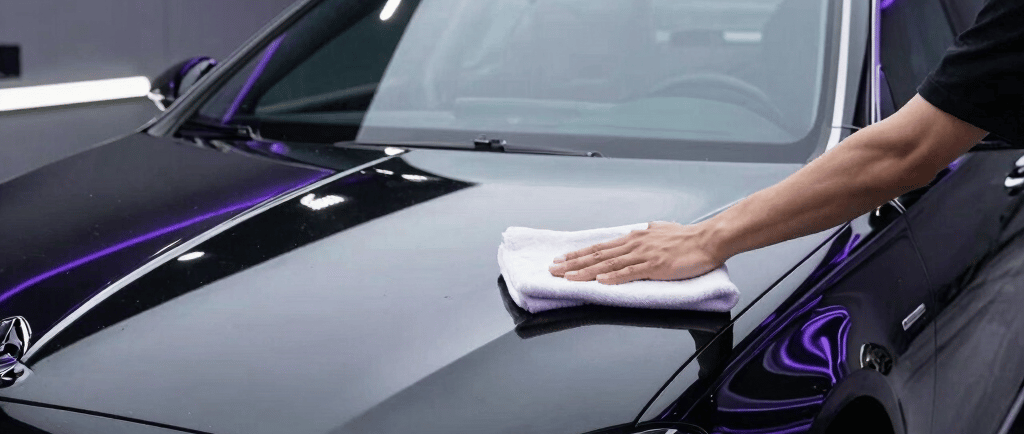 Professional car detailer polishing a black luxury sedan with a microfiber cloth in a detailing studio.
