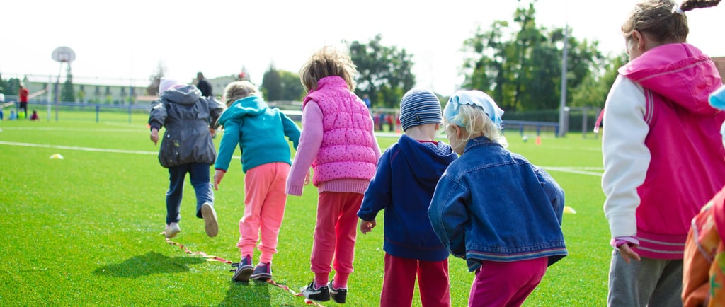 Photo of children standing in a line on a rope laid out on grass in a field