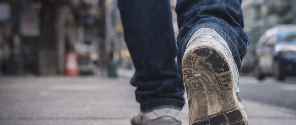 Persona caminando por la ciudad con tenis de uso diario mostrando desgaste en la suela