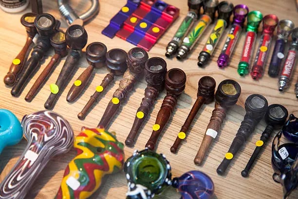 A variety of wooden, glass, and metal smoking pipes displayed on a wooden surface in a head shop.