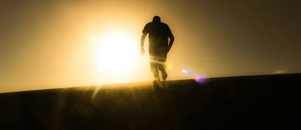 a man walking on a hill with a sun shining through the sun