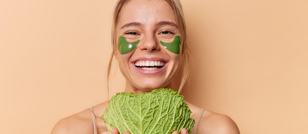 a smiling woman with a vegetable mask on her face and a cabbage leaf in her hands
