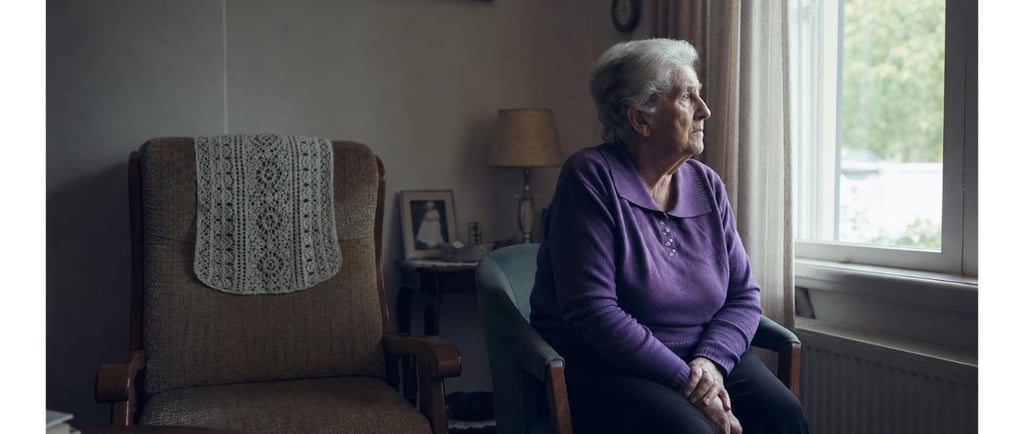 Lonely senior woman sitting alone by a window, a quiet sign of isolation in aging parents