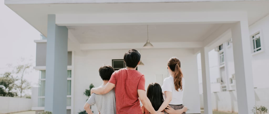Familia abrazada contemplando su vivienda de color blanco