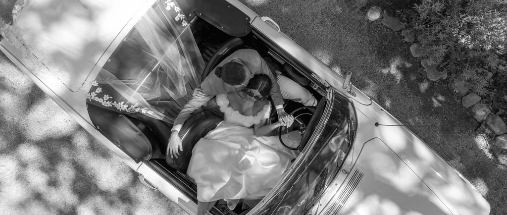 Photo éditoriale en noir et blanc de mariés dans une voiture de collection, chic & cinématographique