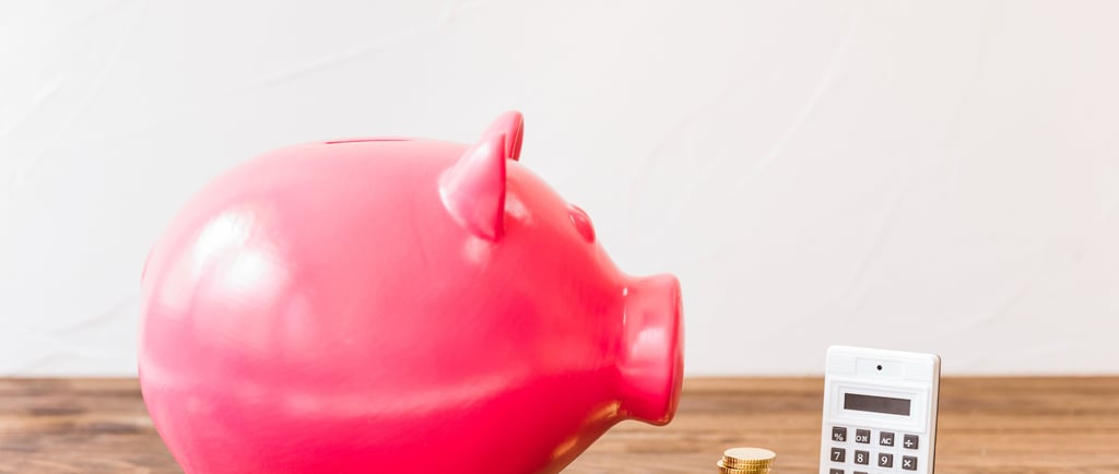 Pink piggy bank with gold coins and a calculator on a wooden table for financial planning.
