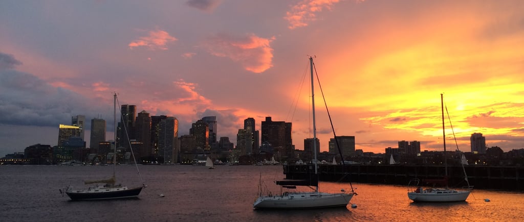 a sunset over a cityscape with boats in the water in Bostonater