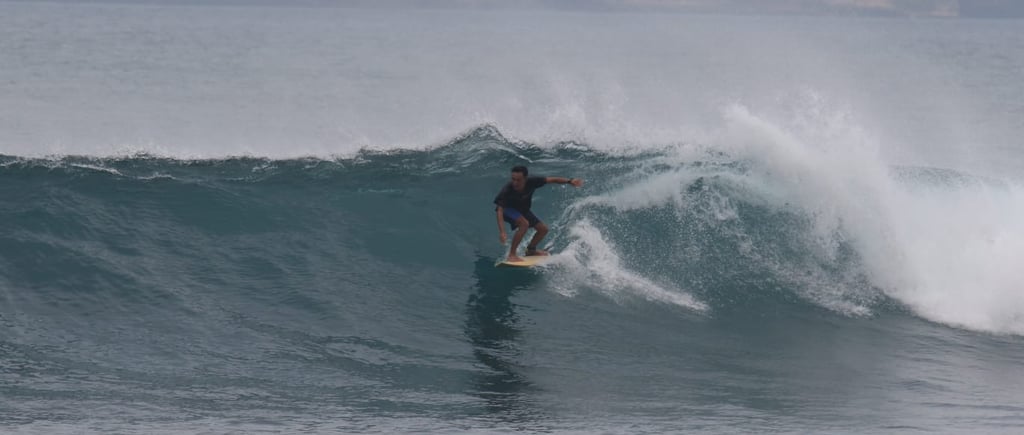 Romi riding a wave while surfing at Ekas beach, showcasing his skills as an experienced instructor.