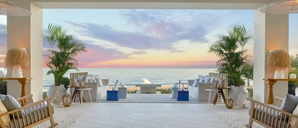 Luxury beachfront patio lounge with outdoor sofas and fire pit at sunset.
