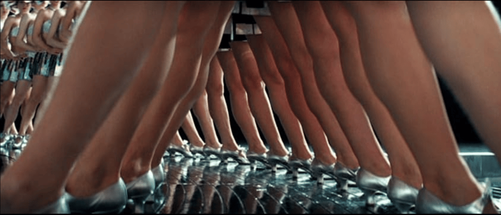 Homage scene from Ken Russell’s The Boy Friend (1971) with silver‑shoed dancers in wide‑leg stance.