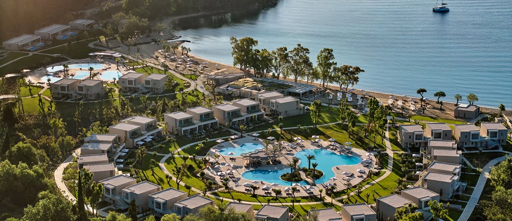 Aerial view of a luxury beachfront resort with circular pools, modern villas, and a private bay.