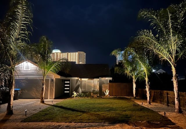 Modern residential home at night with outdoor landscape lighting on palm trees and a green lawn.