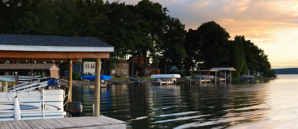 Sunset over a calm lake with boat docks, reflections, and lush green trees along the shoreline.