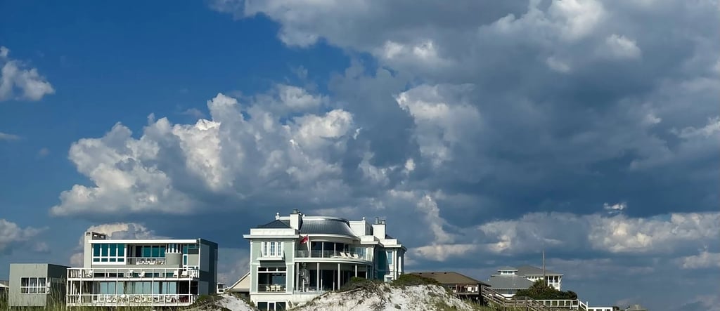Luxury beachfront vacation rentals on white sand dunes under a blue sky with fluffy clouds.