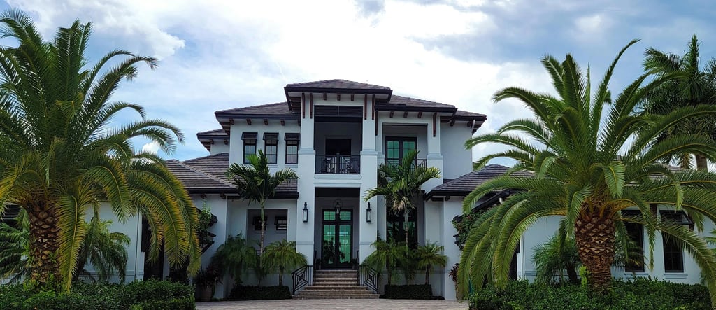 Modern luxury coastal home with a white exterior, brick driveway, and tropical palm tree landscaping.
