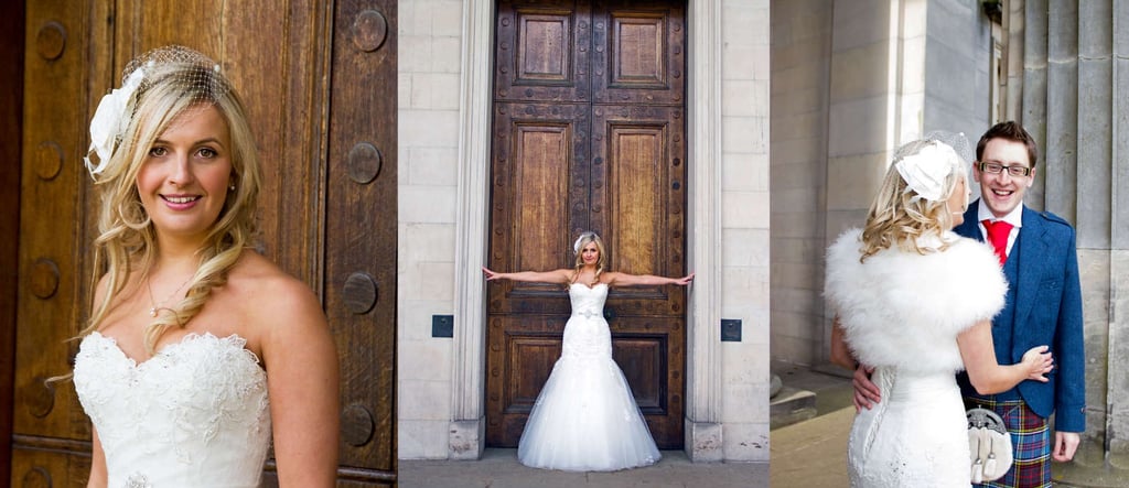 A smiling bride in a lace wedding dress and birdcage veil poses by wooden doors and with her groom in a kilt.