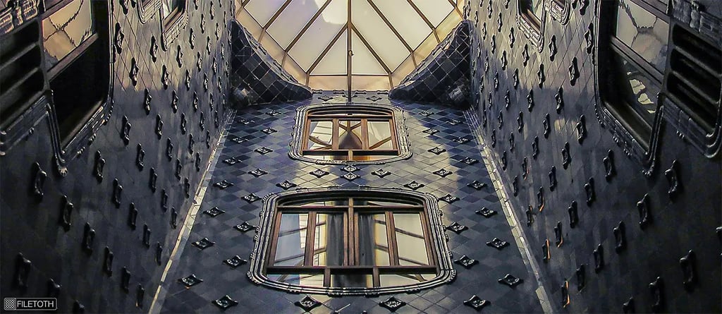 View upward through Casa Batlló’s tiled light well where daylight cascades toward the central skylight.