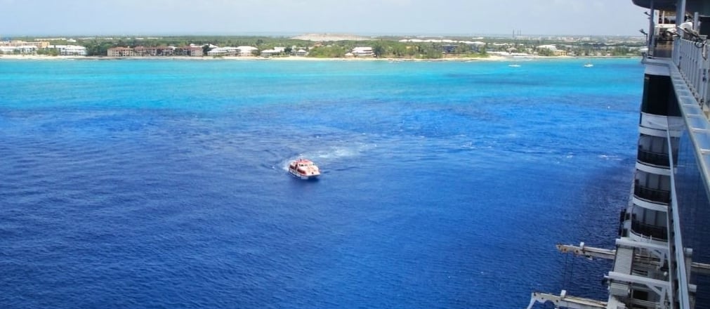Navio de cruzeiro chegando a George Town, Grand Cayman, com o mar azul-turquesa cristalino ao fundo.