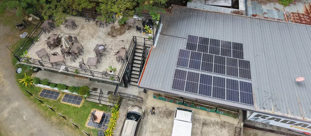 Aerial view of a restaurant with a rooftop patio, parked cars, and solar panels on a metal roof.