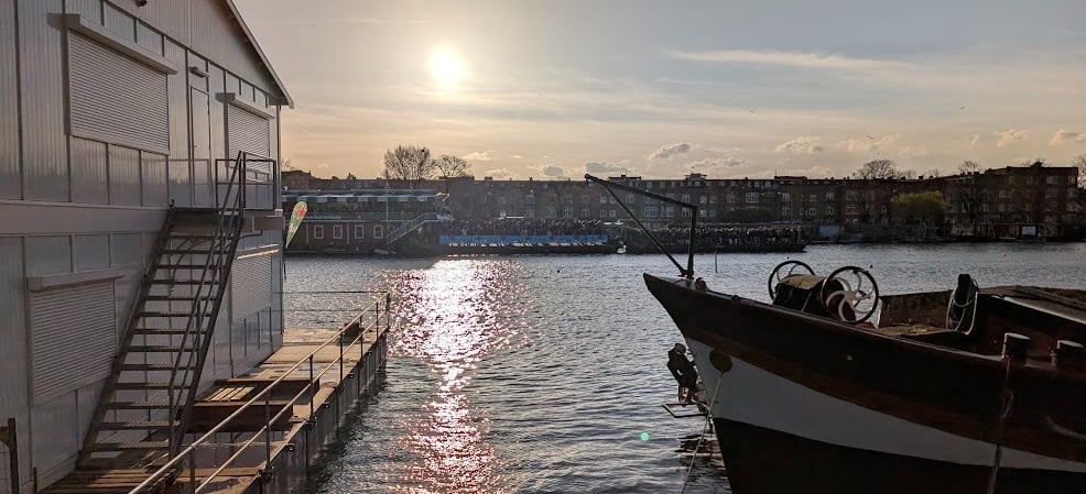Maison flottante moderne et péniche traditionnelle sur un canal d'Amsterdam au coucher du soleil.