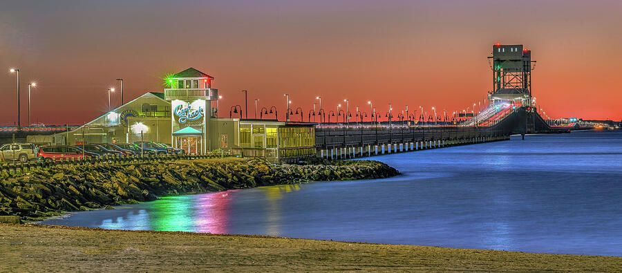 James River Bridge and restaurant at sunset with vibrant orange and purple sky over calm water.