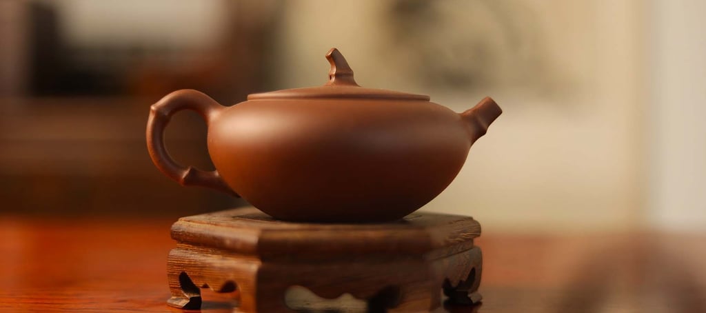 Dark brown, very flat teapot placed on a wooden stand