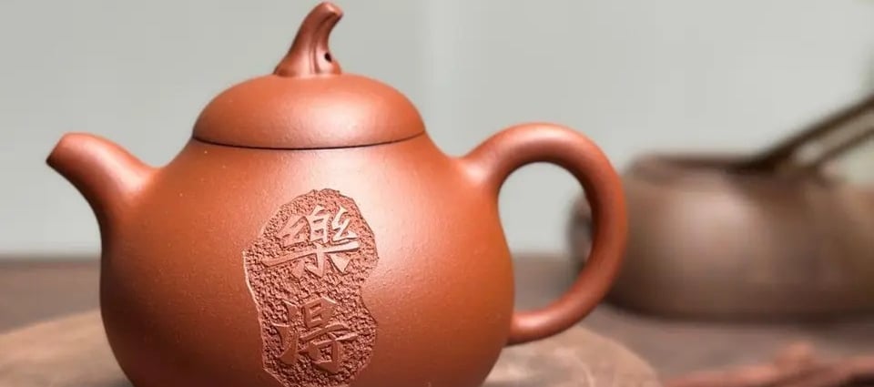 A teapot with engraved text placed on a wooden tabletop