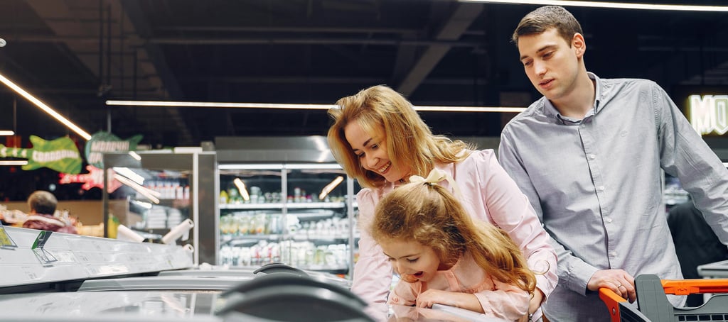 A family choosing frozen food from a grocery store freezer aisle while grocery shopping together.
