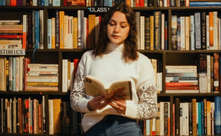 A woman reading a book in front of a library bookshelf