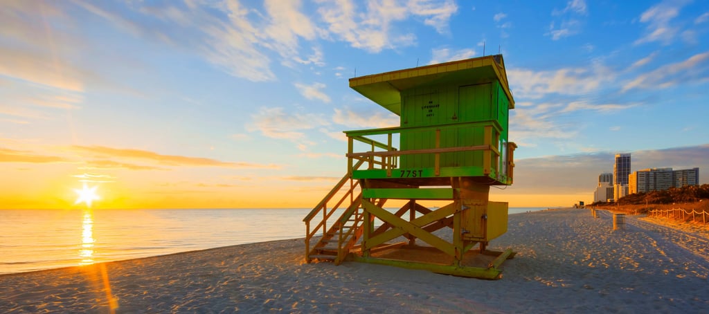 Sunrise over Miami Beach with a green lifeguard stand on the sandy shore and ocean horizon.