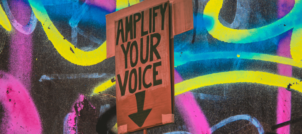 A sign reads "Amplify your voice" over a noisy graffiti background (communication coaching)