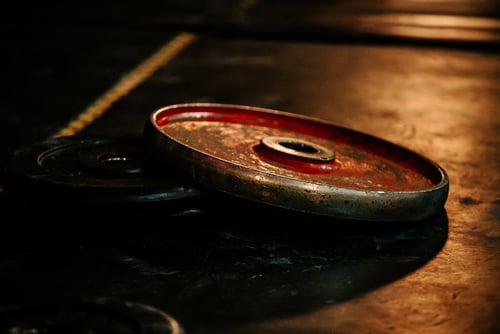 Worn red and black weight plates resting on a dark gym floor with dramatic lighting.