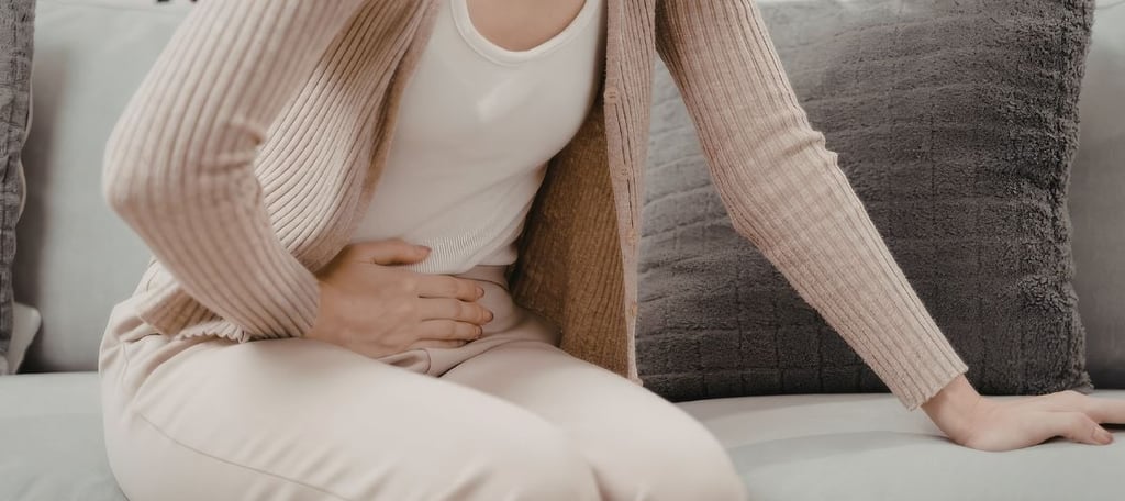 Woman sitting at home holding her stomach, feeling bloated and uncomfortable, representing digestive