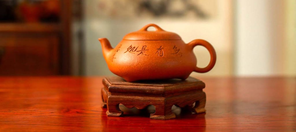 A yellow Yixing teapot engraved with Chinese characters is placed on a wooden stand