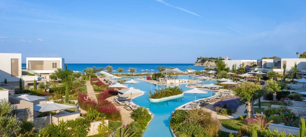 Luxury beachfront resort featuring a sparkling blue infinity pool, white sun umbrellas, and lush gardens overlooking the
