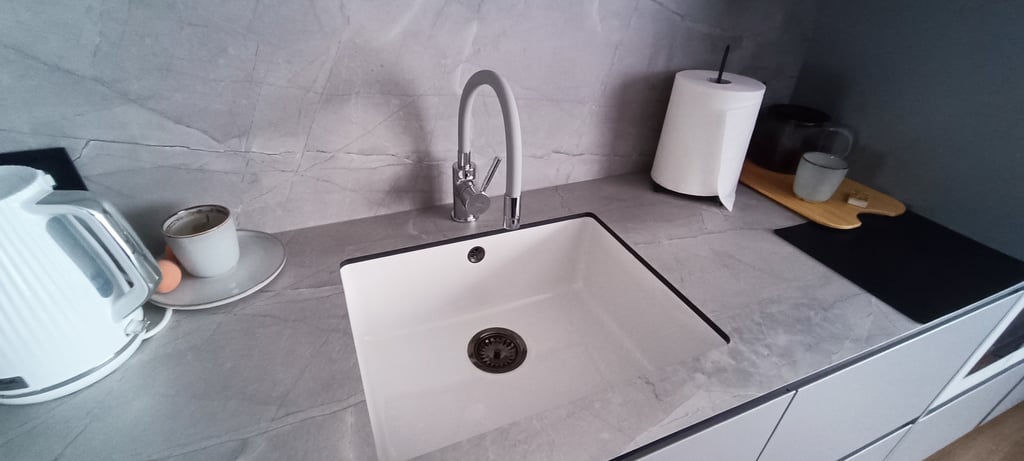 Modern white undermount kitchen sink with a sleek gooseneck faucet on a grey marble countertop.