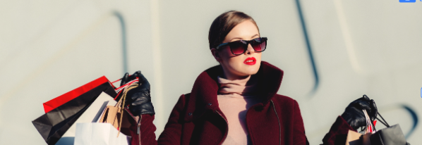 a woman in a red coat and sunglasses holding shopping bags