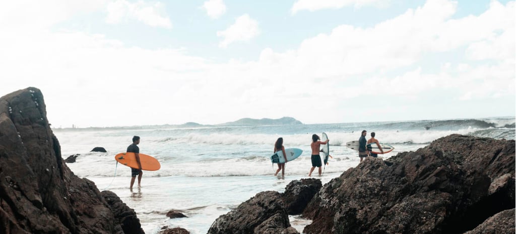 a group of surfing people walking on rocks near the ocean. Byron Bay
