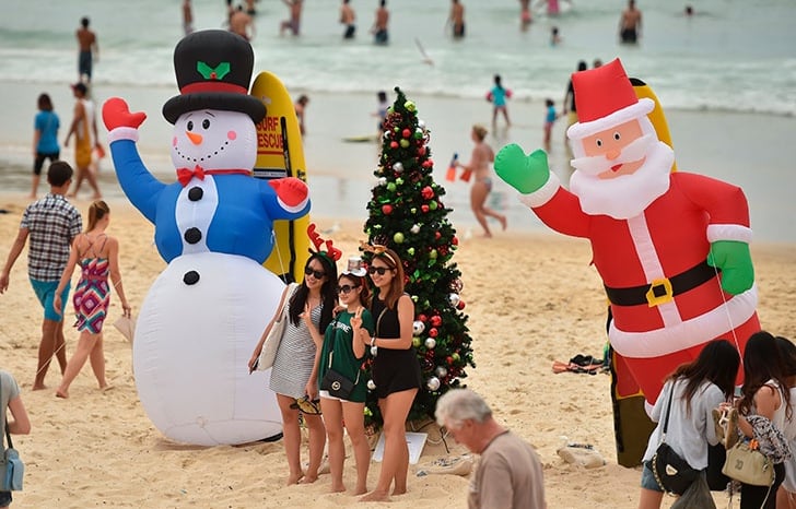 a group of people standing around a christmas tree at the beach in Australia, Christmas celebration