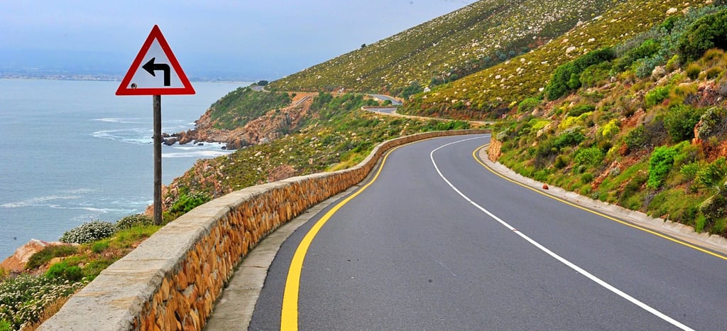 Estrada costeira para Gordon’s Bay na Cidade do Cabo, com montanha de um lado e o mar do outro.