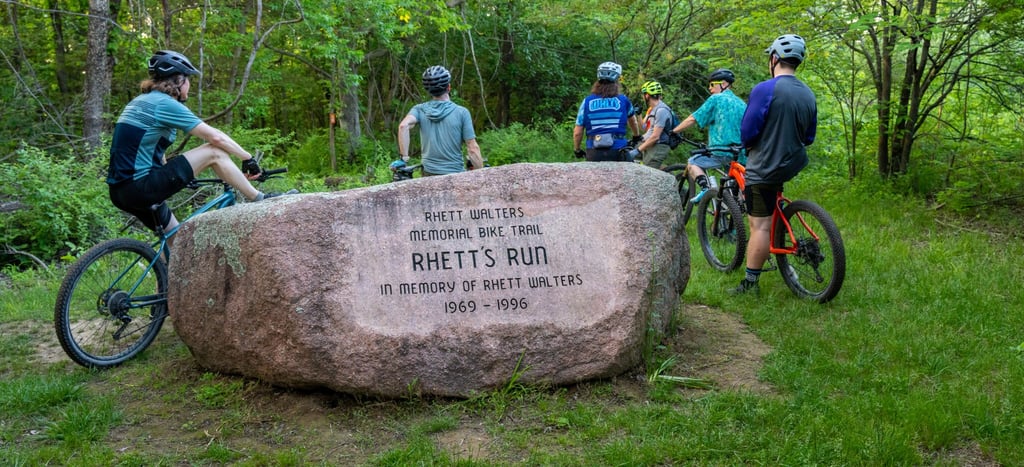 People stopped on their bikes next to a large rock engraved with the memorial info of "Rhett's Run"