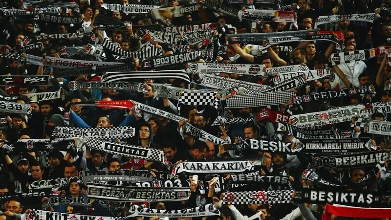 Beşiktaş-Fans in schwarz-weißen Farben jubeln und schwenken Fahnen im Stadion.