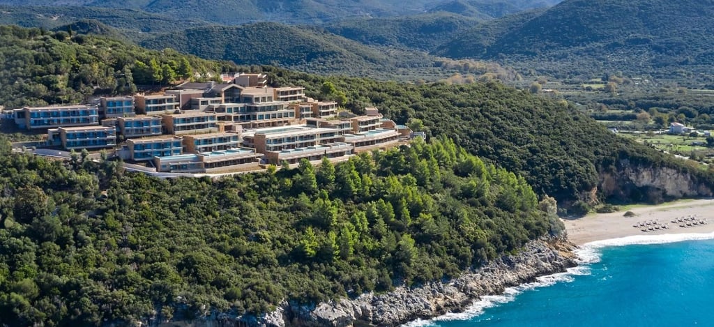 Luxury hillside resort overlooking the turquoise Ionian Sea and lush green mountains in Greece.