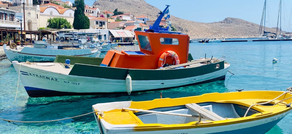 Traditional fishing boats floating on turquoise water at Halki island harbor in Greece.