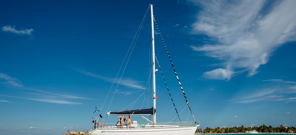 A white sailboat with two people on deck glides across turquoise ocean water under a clear blue sky, capturing the essence